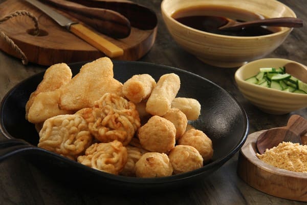 Sebuah hidangan pempek Palembang lengkap dengan kuah cuko, irisan timun, dan bubuk cabe sebagai hiasan.
