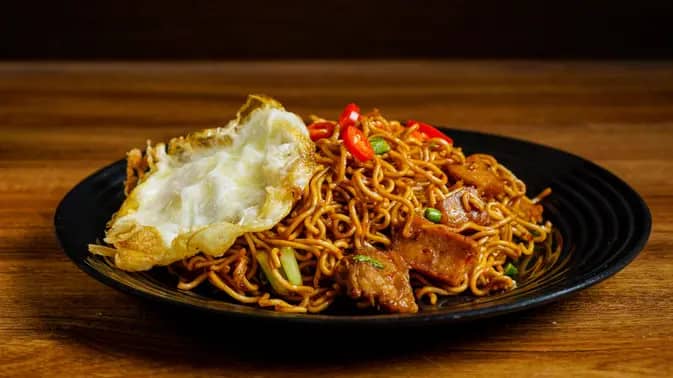 Sepiring mie goreng pedas dengan taburan cabai merah dan topping ayam suwir