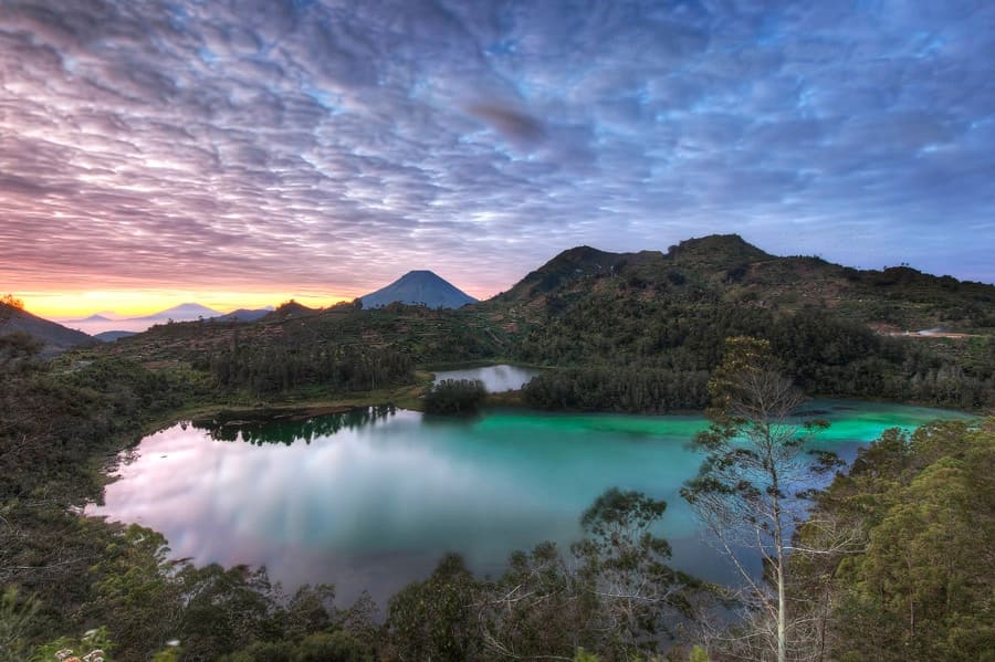 Hikers on Mount Sikunir observing a breathtaking sunrise panorama over mist-covered hills.