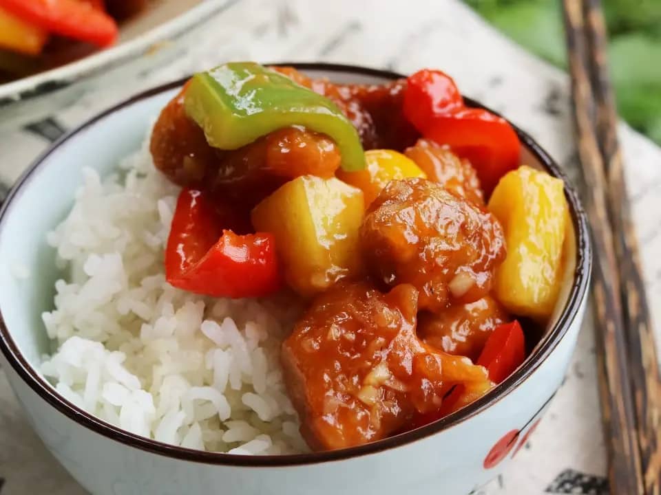 Sweet and Sour Pork served over steamed white rice, garnished with green onions